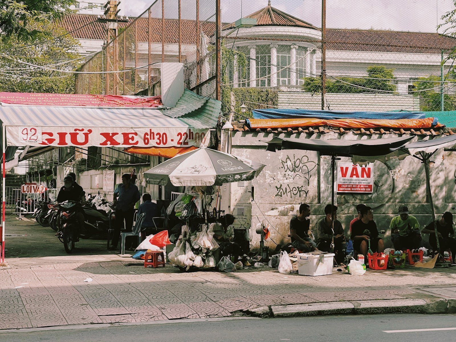 Vỉa hè đô thị Việt Nam với hàng cây, quán xá và xe dựng bên dưới