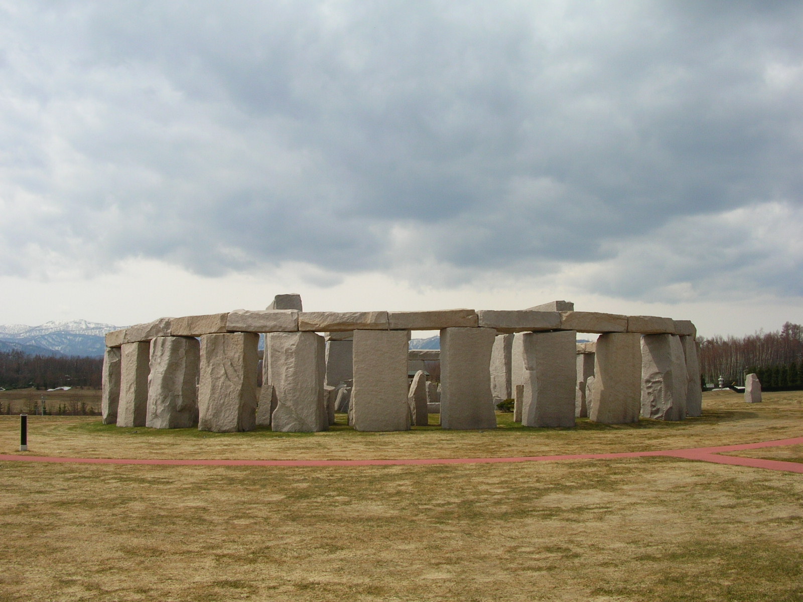Vòng đá dựng theo Stonehenge tại nghĩa trang Makomanai Takino, nền cỏ úa và núi tuyết phía xa