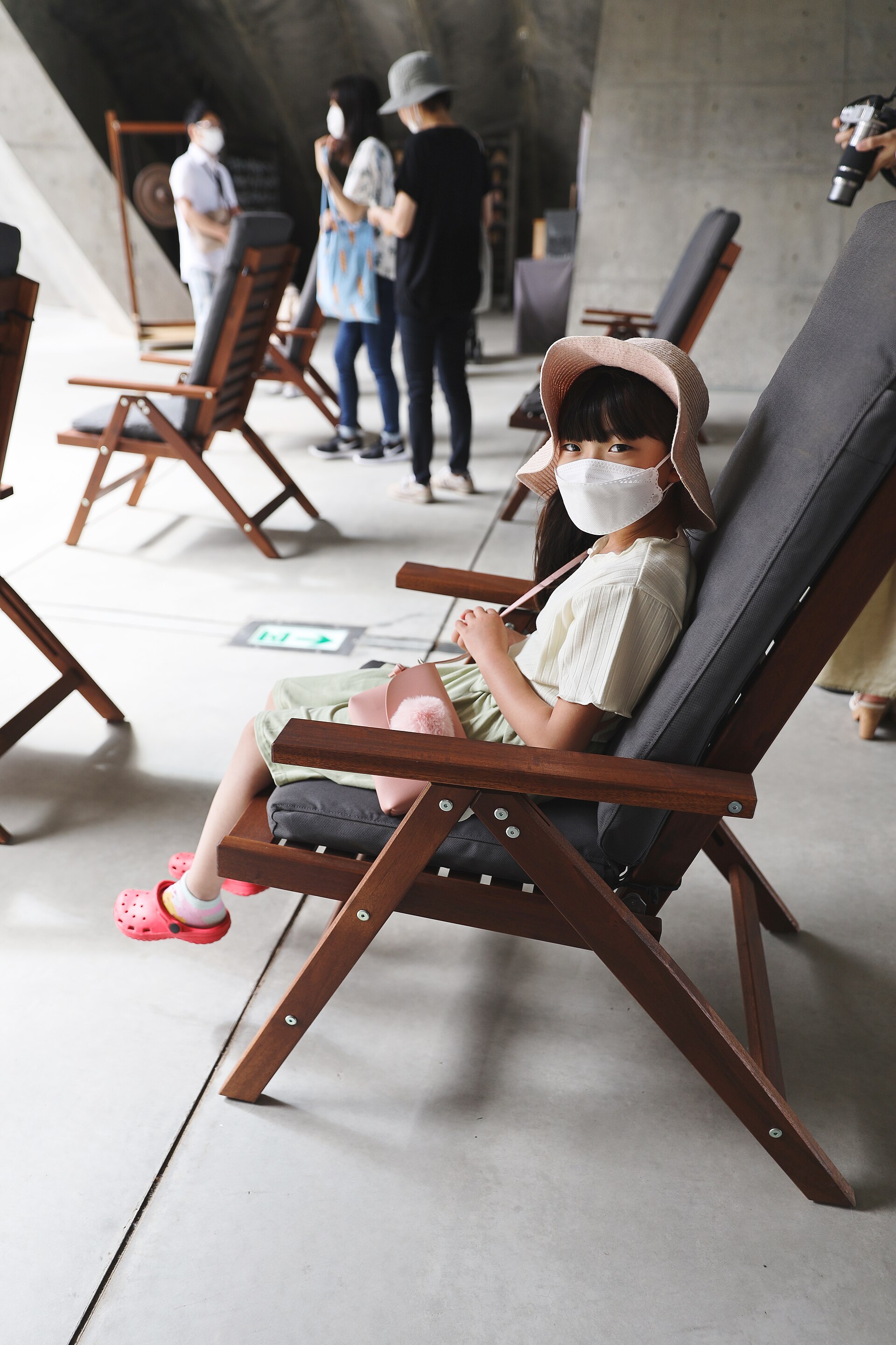 Ghế gỗ đặt dưới vòm bê tông của Hill of the Buddha cho khách ngồi nghỉ, du khách đeo khẩu trang xung quanh
