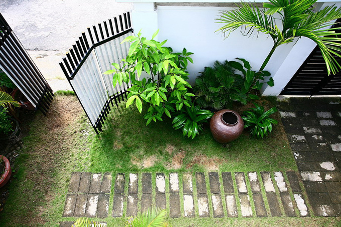 Một khoảng sân trước với những mảng xanh nho nhỏ, cây cau, chum nước gợi hình ảnh thôn quê.