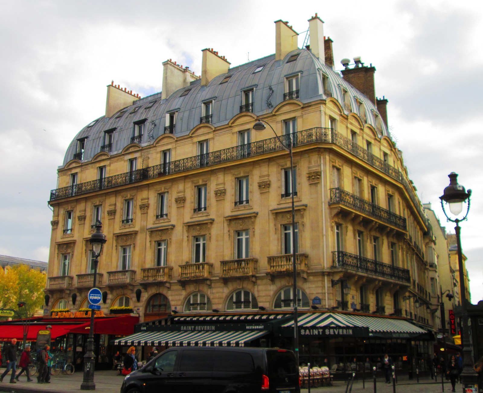 Toà nhà kiểu Haussmann ở một góc phố Paris, mái đá xám dốc, ban công sắt, mặt tiền đá cắt đều tầng