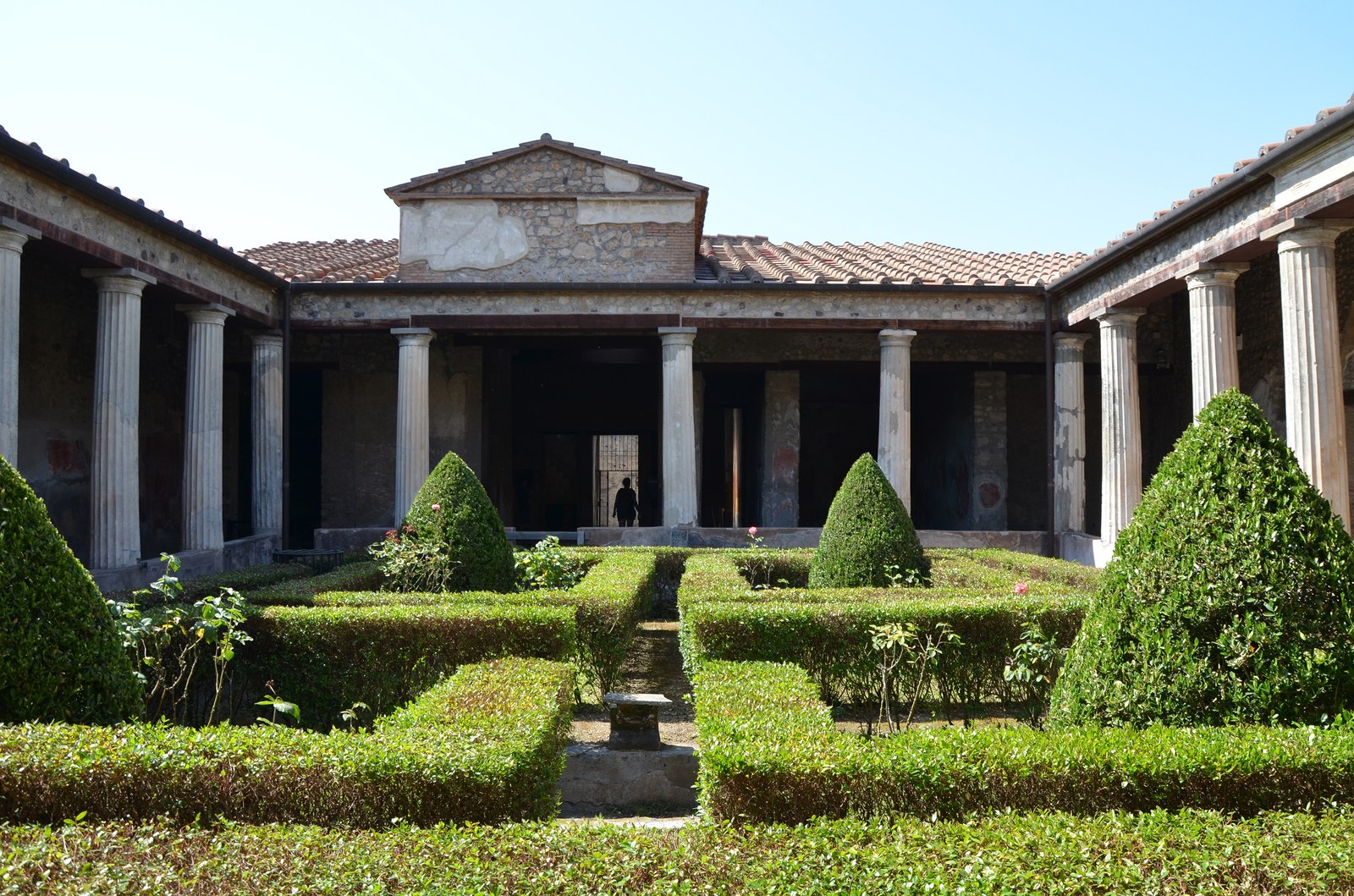 Sân peristyle của một nhà phố La Mã ở Pompeii, hành lang cột đá vôi bao quanh khu vườn hình chữ nhật có hàng cây bụi cắt hình tháp và luống hoa hồng