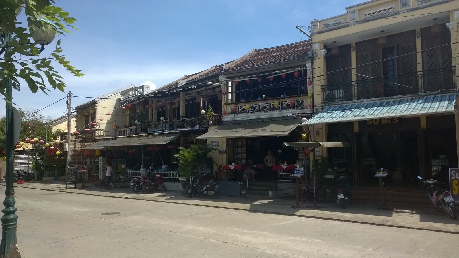 Một đoạn phố mua sắm ở Hội An với dãy nhà hai tầng mái ngói, đèn lồng nhiều màu treo dọc ban công, người đi bộ trên vỉa hè