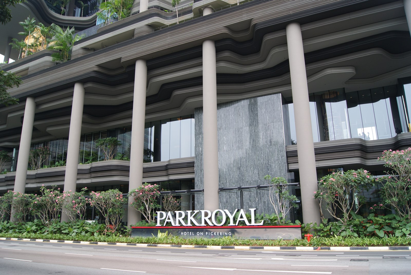 Cận cảnh biển hiệu "PARKROYAL Hotel on Pickering" ở lối vào, cây và bồn hoa trồng ngay dưới đất hai bên biển hiệu