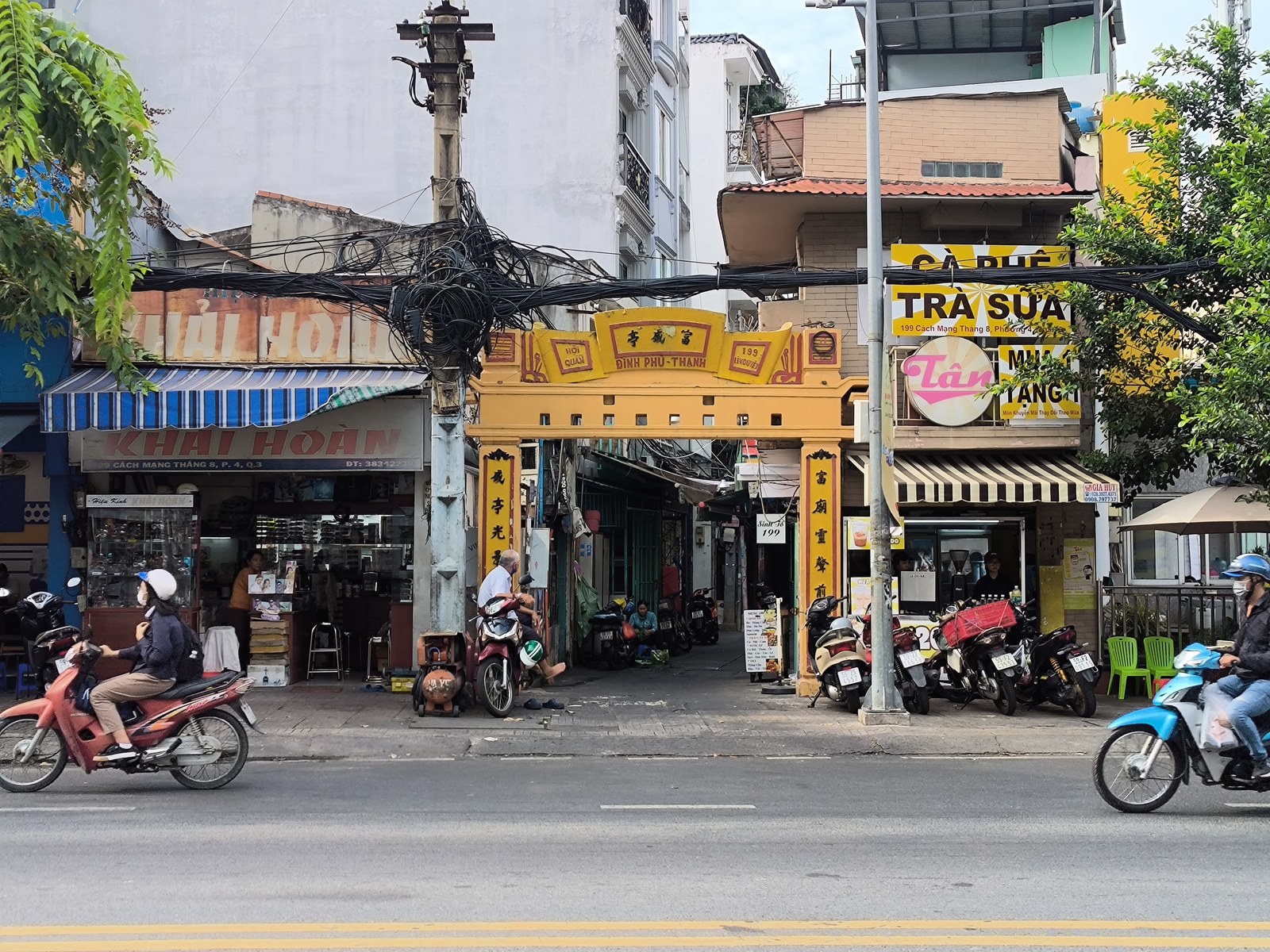 Cổng tam quan màu vàng của Đình Phú Thạnh nằm lọt giữa hai dãy nhà phố với biển hiệu quán ăn, cà phê, dây điện chằng chịt phía trên