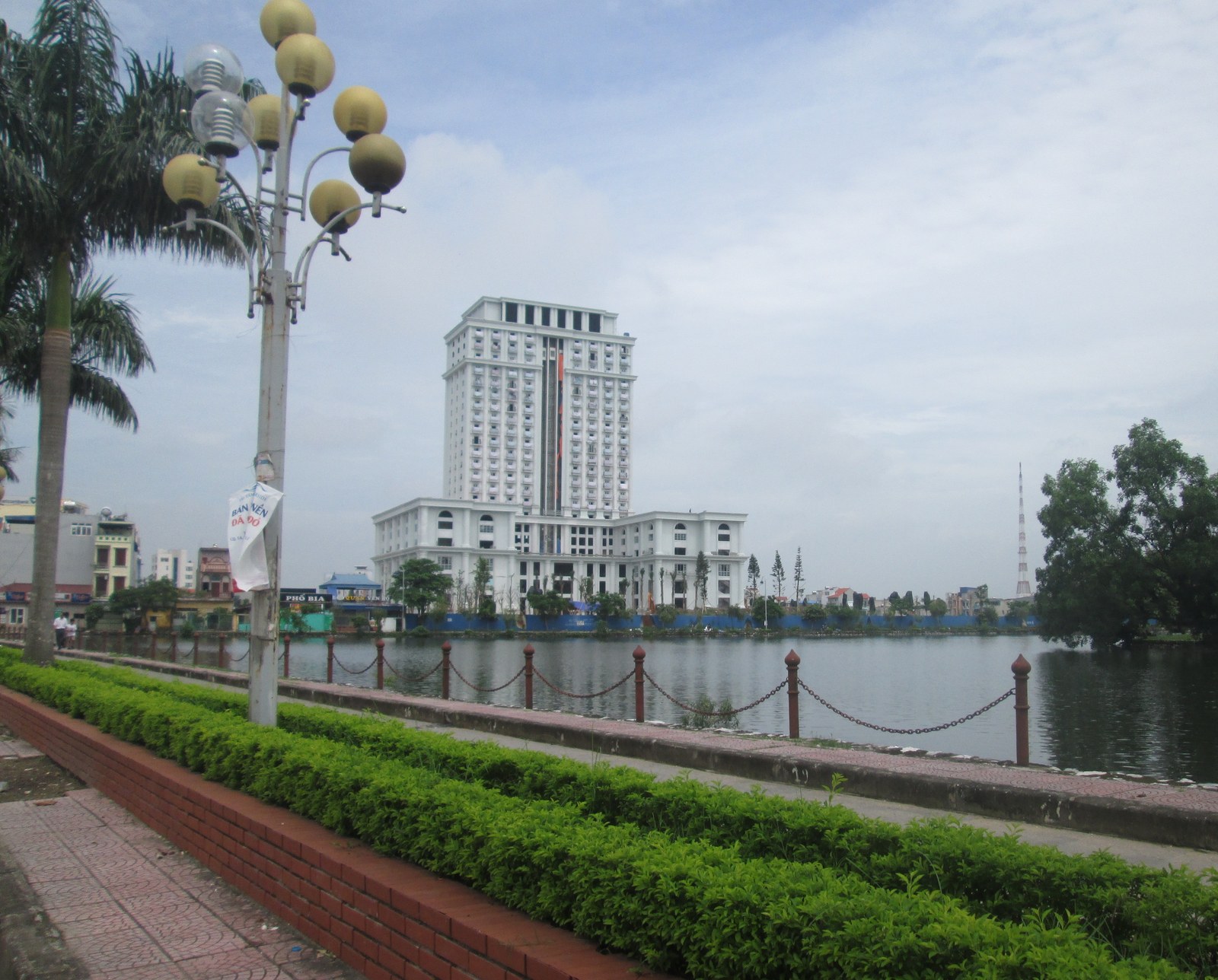 Một khách sạn cao tầng đứng cạnh hồ nước trong khu đô thị, đèn đường kiểu cổ điển ở tiền cảnh