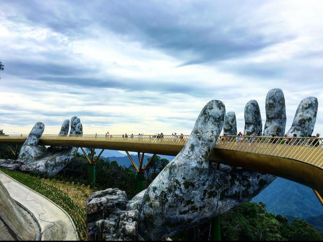 Cận cảnh hai bàn tay đá đỡ mặt cầu nhìn từ phía dưới lên, nền trời nhiều mây