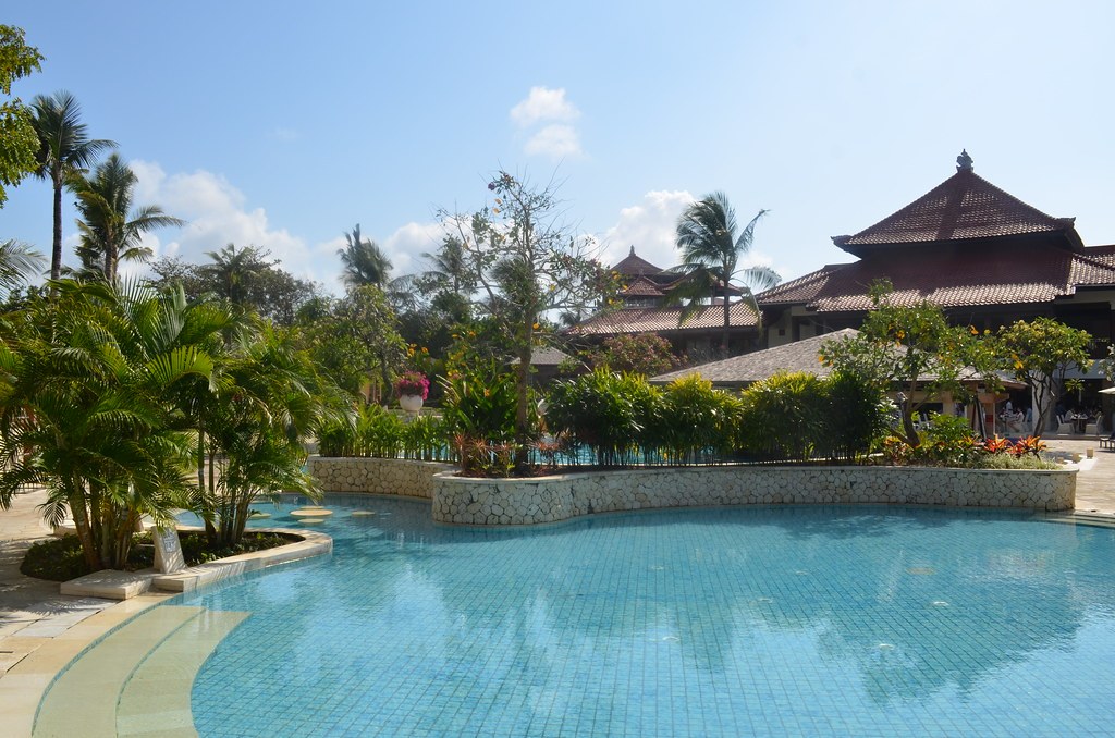 Hồ bơi uốn lượn trước một quần thể kiến trúc mái ngói kiểu Á Đông, cây dừa bao quanh