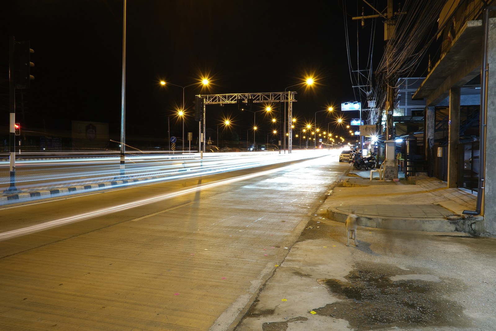 Con phố về đêm vắng người, đèn đường sáng đều hai bên, ánh sáng kéo vệt dài do phơi sáng lâu.