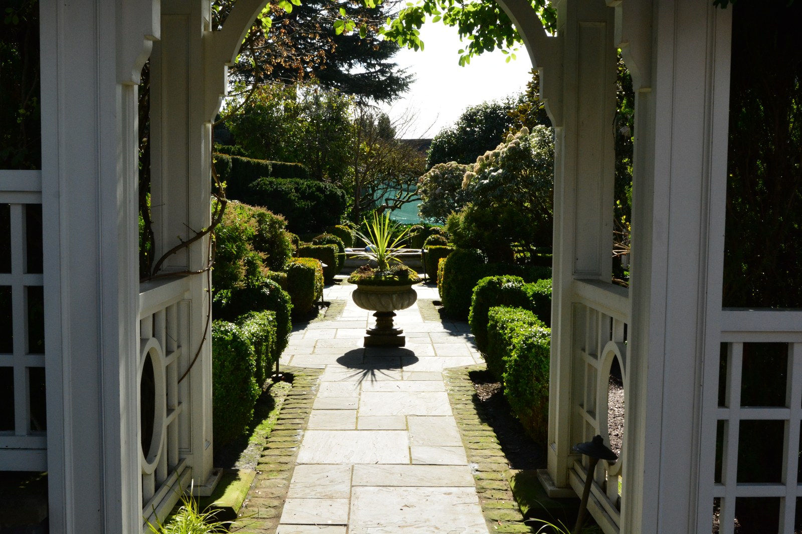 Nhìn từ trong một mái vòm gỗ trắng ra một lối đi lát đá thẳng, hai hàng cây bụi xén vuông hai bên, cuối lối đi là một chậu đá lớn đặt cây, xa hơn thấp thoáng mặt nước xanh